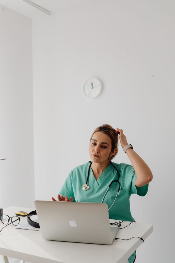 A female doctor in green scrubs conducts a virtual consultation from a modern office.