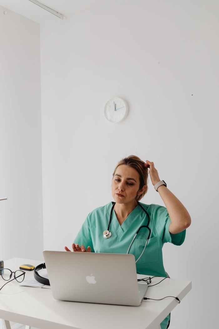 A female doctor in green scrubs conducts a virtual consultation from a modern office.